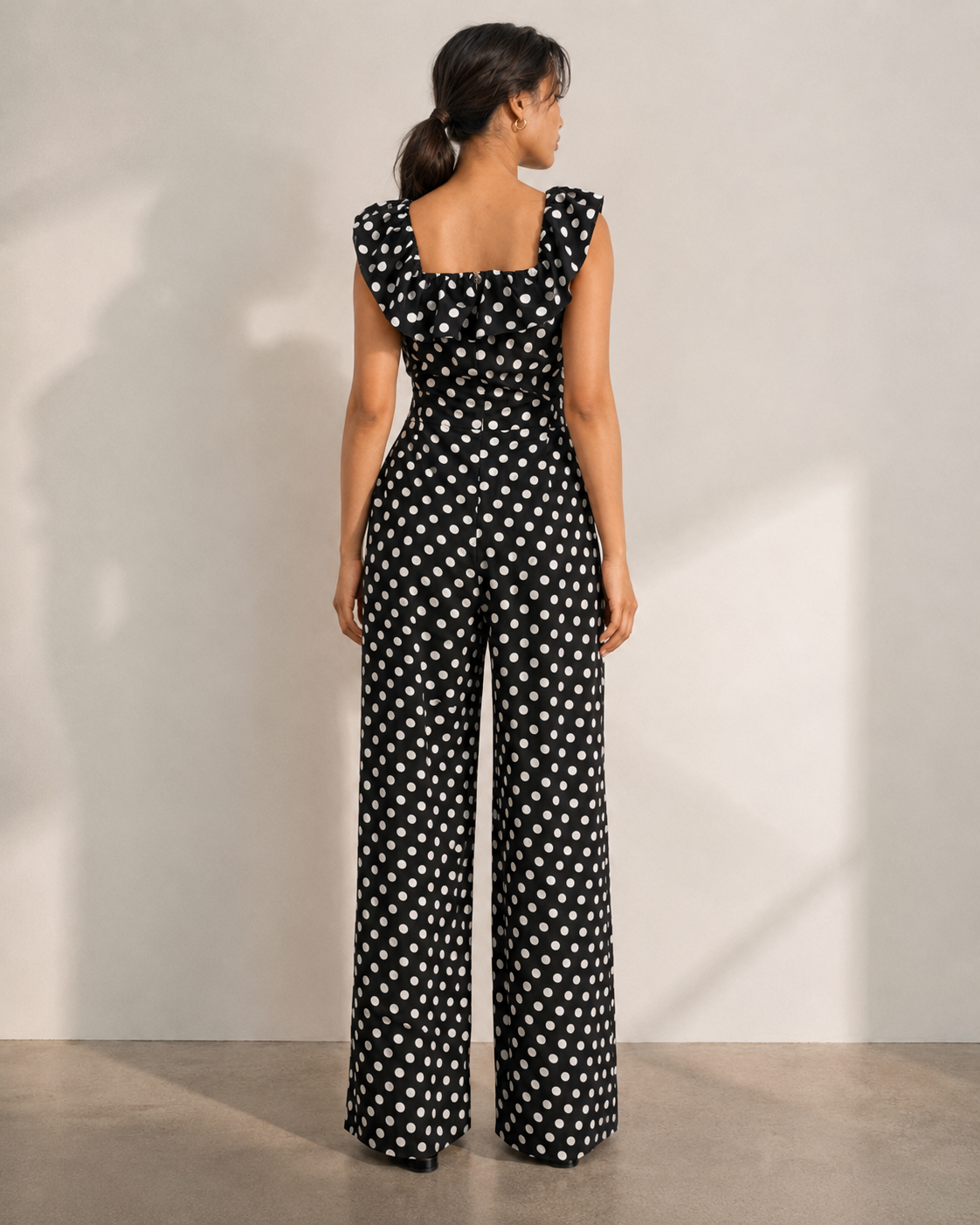 Back view of the ISLA black polka dot jumpsuit showing the ruffle across the back neckline.