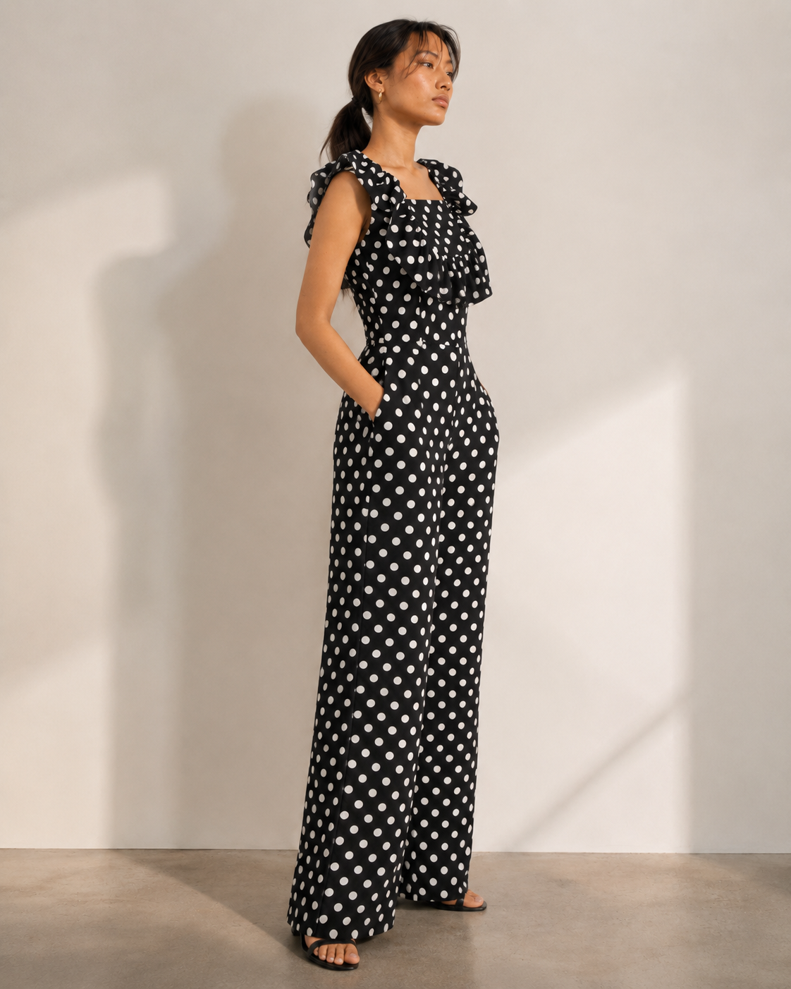 ISLA black jumpsuit with white polka dots, ruffled square neckline and wide legs.