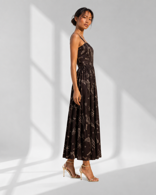 NYALA black safari print midi dress in profile, slim straps and a full ankle-grazing satin skirt.